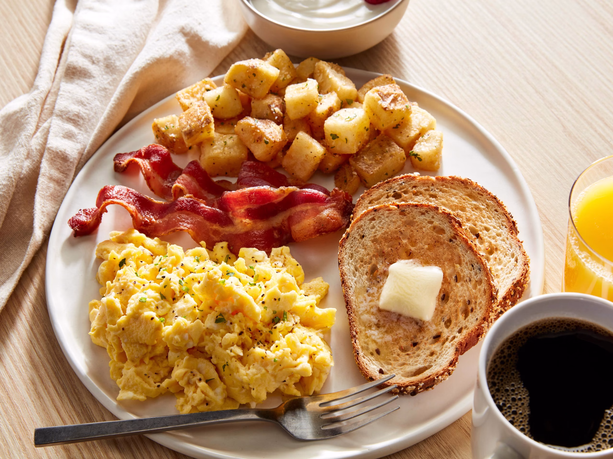 Plate of scrambled eggs, crispy bacon, breakfast potatoes, and multigrain toast with butter, served with orange juice and coffee at Rooh Nashville.