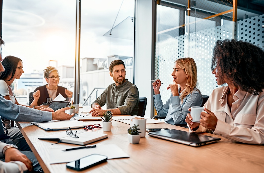Business professionals having a team meeting in a modern conference room with large windows and natural light.