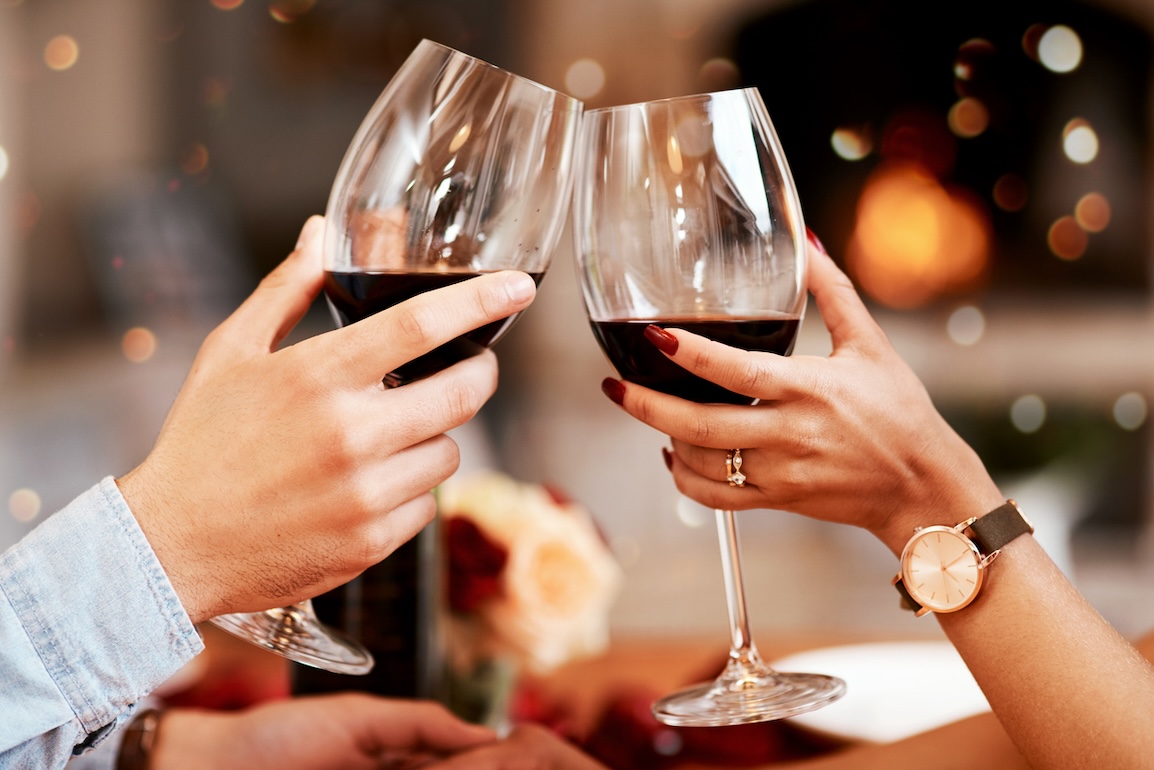 Close-up of a couple toasting red wine glasses during a romantic dinner, with soft lighting and a cozy atmosphere.