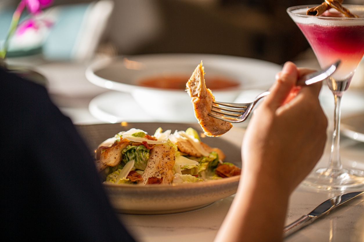 Woman enjoying a fresh salad and cocktail at a restaurant table, highlighting a relaxed dining experience near Nashville Airport.