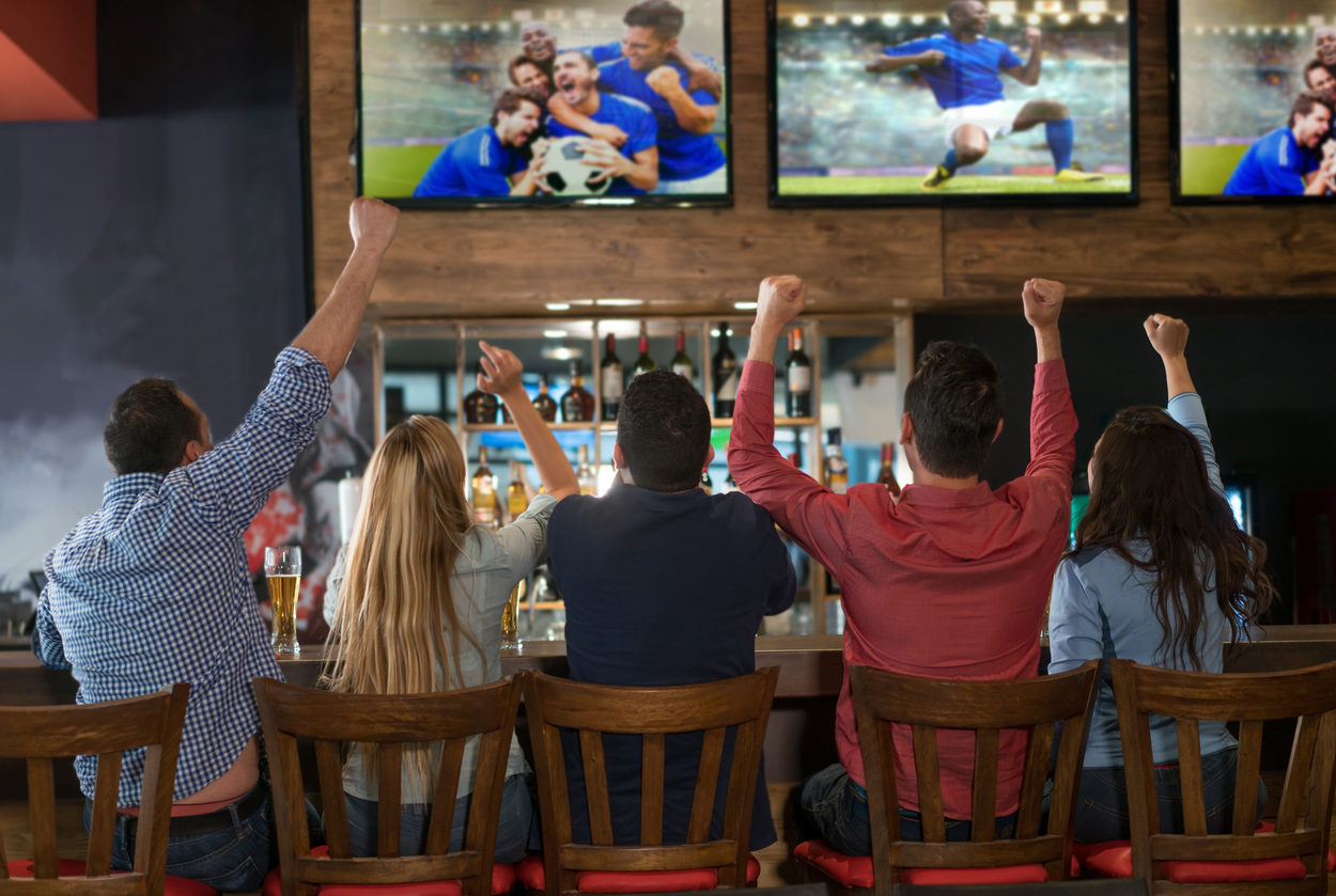 Fans enjoying game night at a sports bar near Nashville Airport with food and drinks on the table.