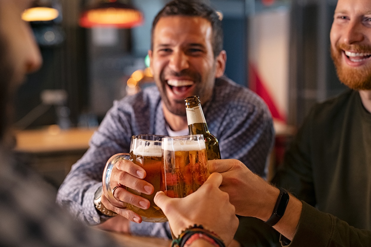 Friends toasting beer at a bar, smiling and enjoying drinks in a relaxed restaurant setting—perfect for a hotel bar atmosphere near Nashville Airport.